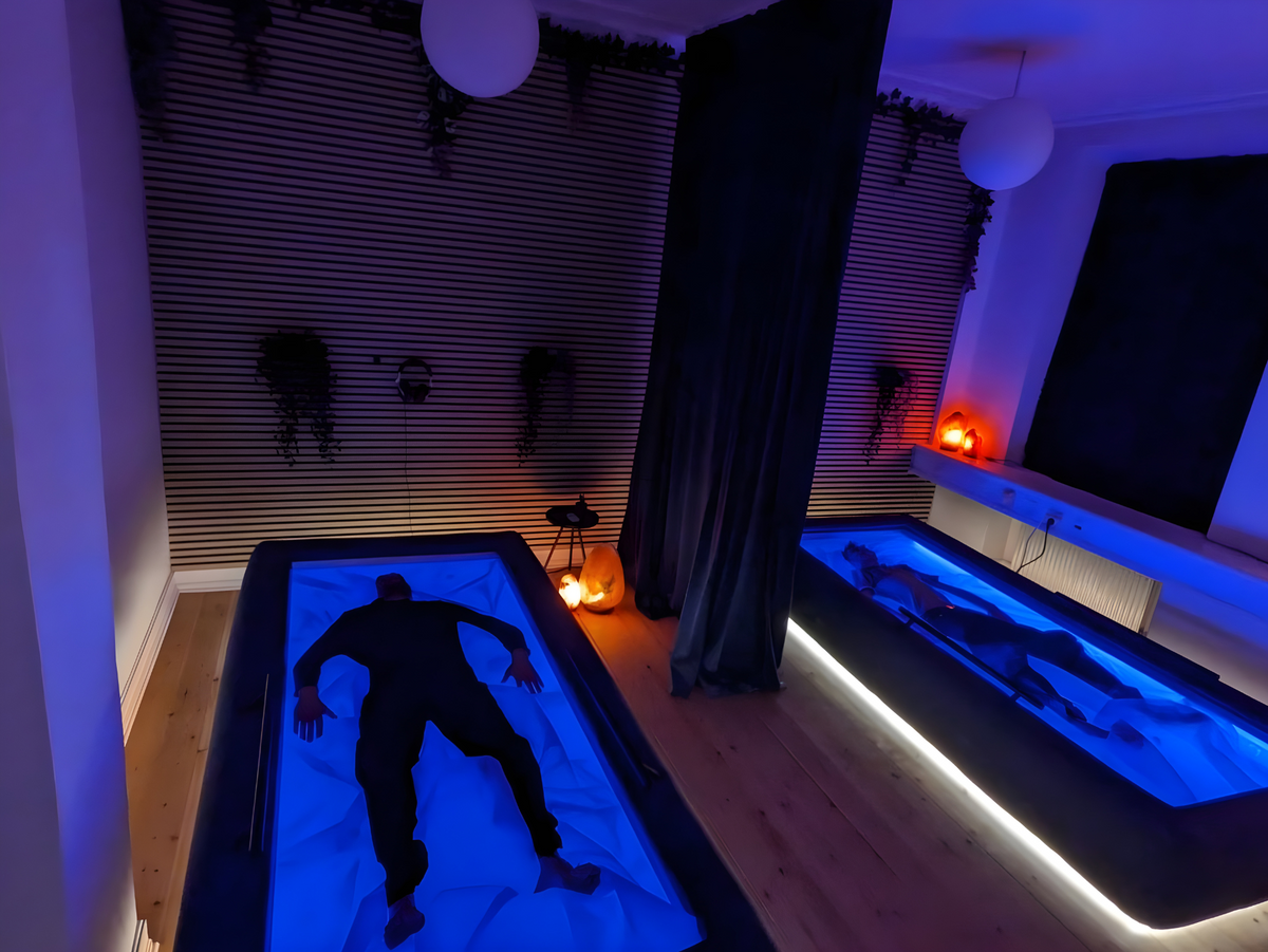 Two people lying in separate blue-lit Driifloat beds with a curtain between them.