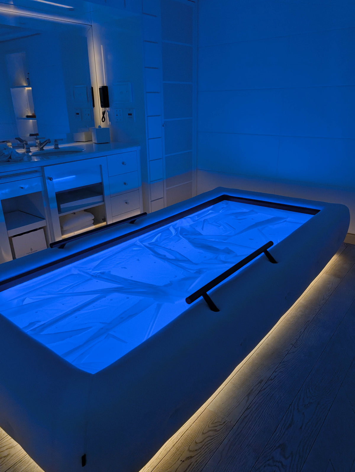 Blue-lit Driifloat bed with black support rails and warm underlighting beside white cabinets.